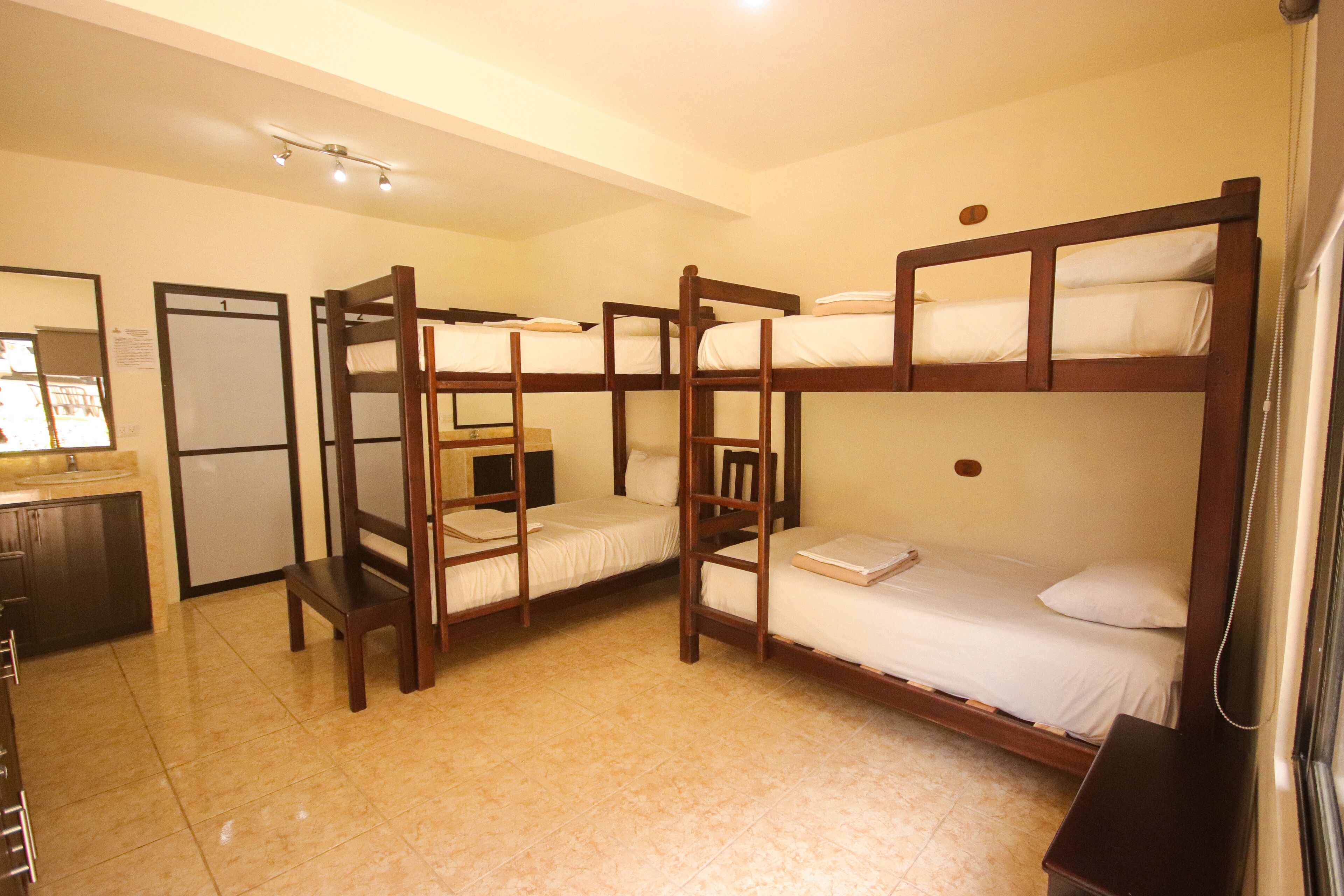 A dormitory room with bunk beds, a desk, and a small kitchenette.