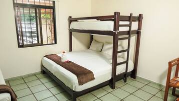 Uma cama beliche com janela, uma cadeira e piso ladrilhado.