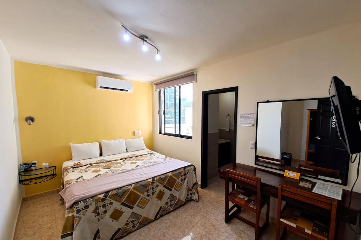 A bedroom with a bed, bedside table, desk, chair, and a large mirror.