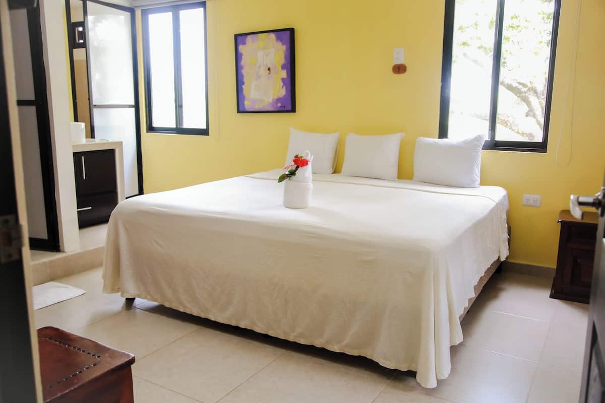 A hotel room with a large bed, a painting on the wall, and a window with a view of trees.