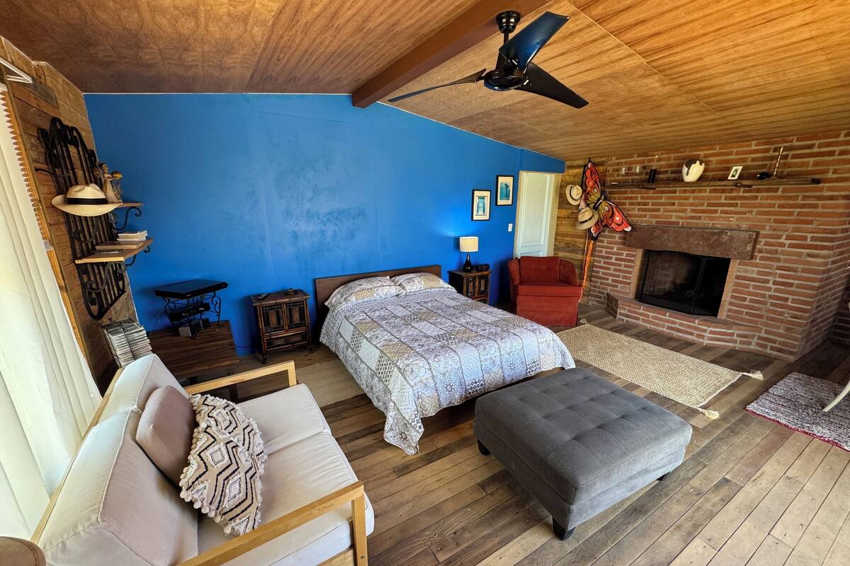A bedroom with a large bed, a wooden ceiling fan, a brick fireplace, and a blue accent wall.