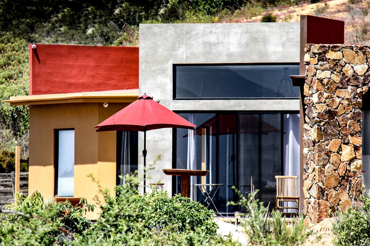 A modern house with a red roof, a stone wall, and a patio with a red umbrella.
