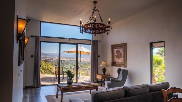 A spacious living room with a large window, a chandelier, and a view of the outdoors. - Rancho Cien Piedras (Valle de Guadalupe)