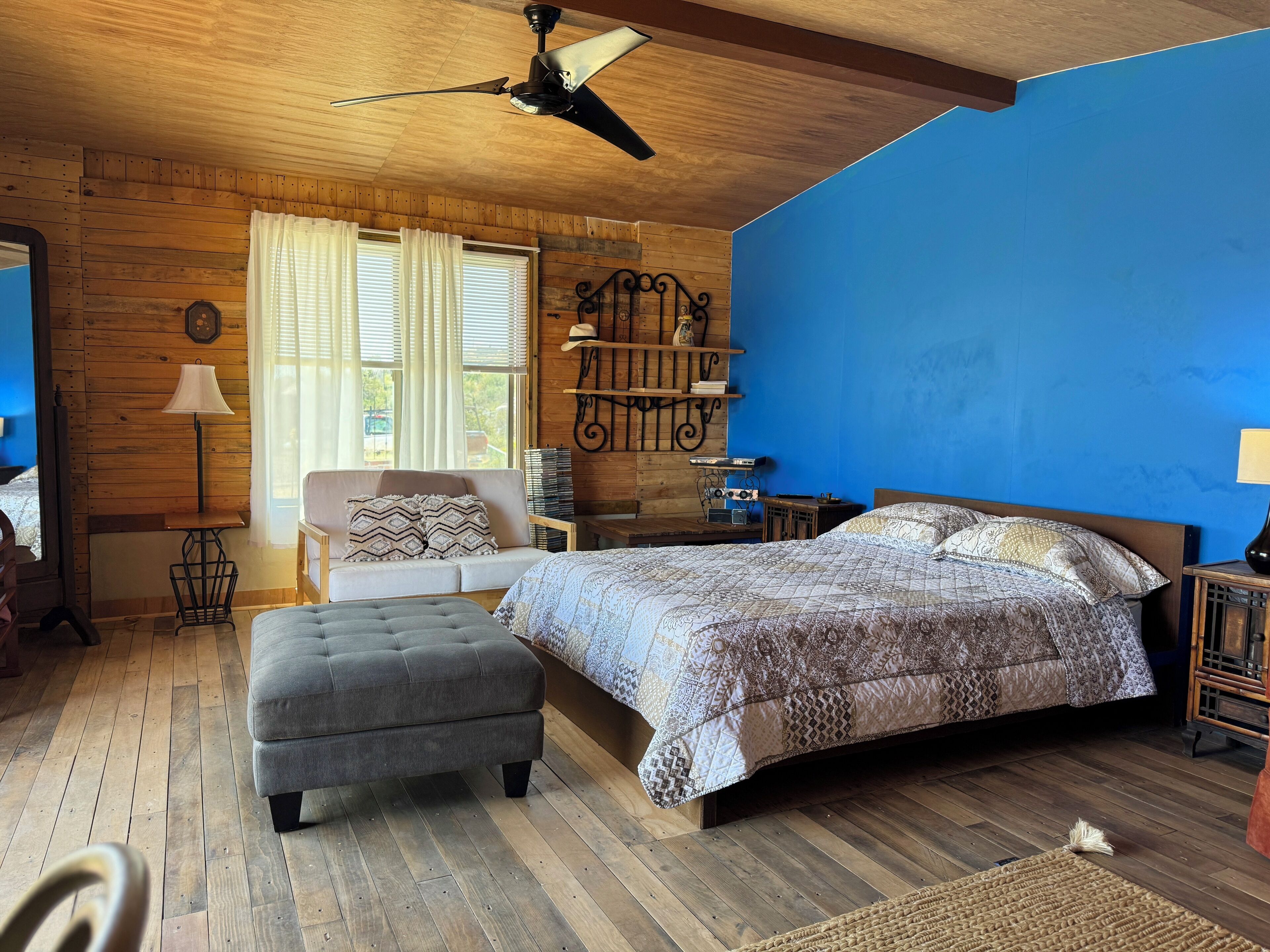 A cozy bedroom with a large bed, a sofa, a wooden ceiling, and a blue accent wall.