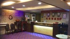 A hotel reception area with a carpeted floor, a reception desk, chairs, and a wall with clocks and a sign. - Hone Lane Business Hotel (Kaohsiung)