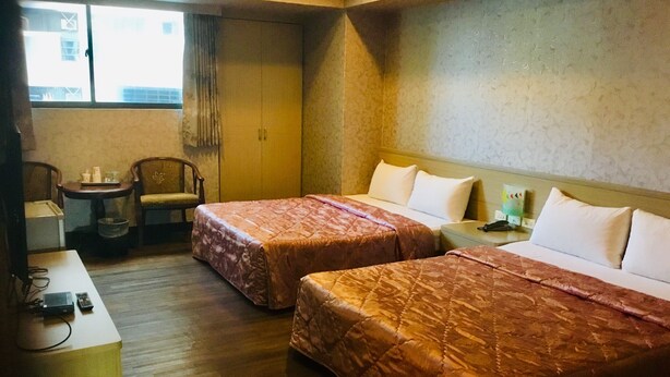 A hotel room with two beds, a small table with a chair, a desk with a telephone, and a window with curtains. - Hone Lane Business Hotel (Kaohsiung)