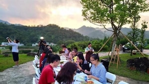 Un grupo de personas cenando al aire libre con montañas al fondo.