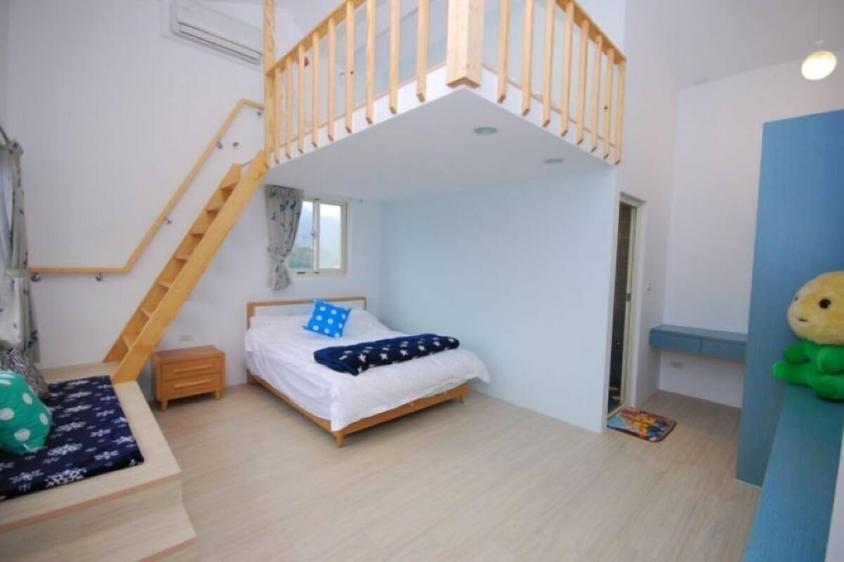 A bedroom with a wooden bunk bed, a small bedside table, a window with curtains, and a blue wall.
