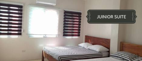 Una suite junior con dos camas, un cabecero de madera y una ventana con persianas.