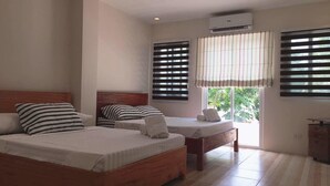 A bedroom with two beds, a wooden headboard, striped pillows, a window with blinds, and an air conditioning unit. - Hotel Lady Nina (Baler)