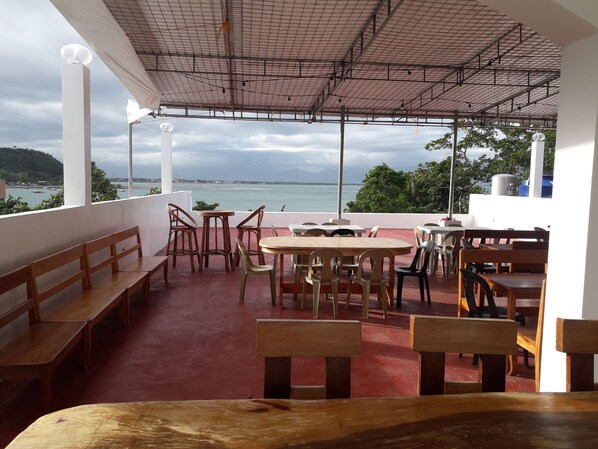 An outdoor seating area with wooden benches and tables, overlooking a body of water and a distant coastline. - Hotel Lady Nina (Baler)