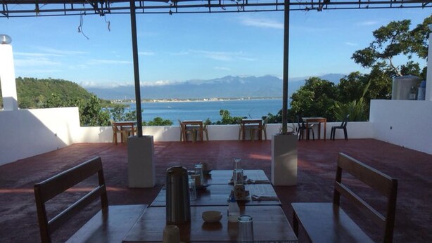 An outdoor dining area with a table set for two, overlooking a scenic view of the sea and mountains. - Hotel Lady Nina (Baler)
