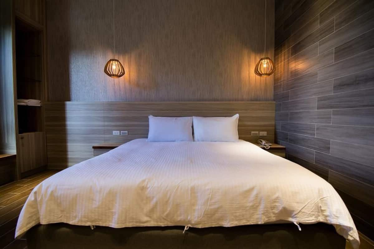 A large bed with a wooden headboard, two bedside lamps, and a wooden floor.