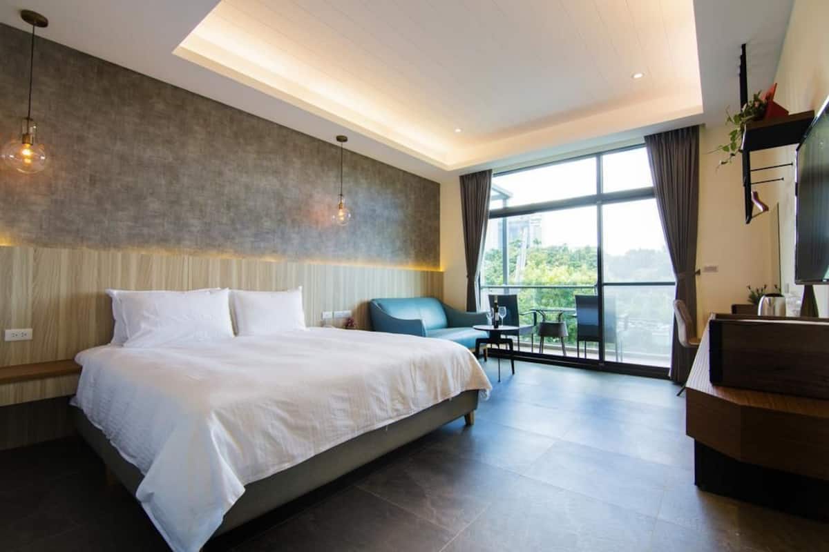 A modern hotel room with a large bed, a seating area with a table and chairs, and a balcony with a view.