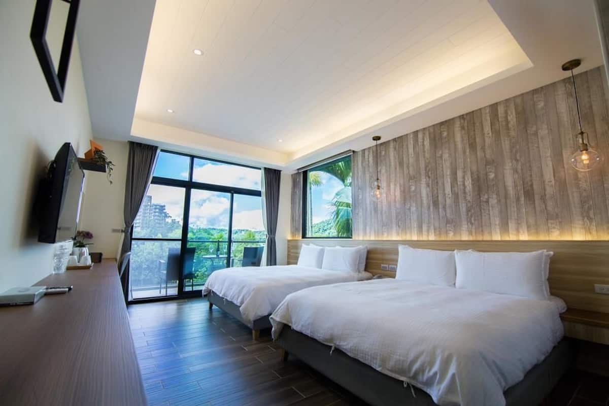 A modern hotel room with two beds, a large window offering a view of greenery, and a wooden accent wall.