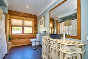 Bathroom features a distressed vanity, black basin, and large mirror above a wooden wall paneling.