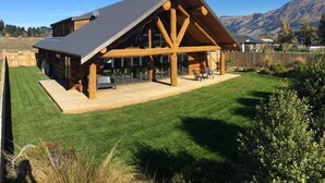 Een vakantiehuis van hout met een ruim terras, omgeven door een verzorgd gazon en bergen op de achtergrond.