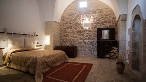 Una camera da letto con parete in pietra, un letto con copriletto decorato, una cassettiera e uno specchio.