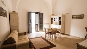 Un'ampia zona giorno con divano, tavolo da pranzo con sedie e angolo cottura con pensili.