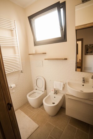 Une salle de bain comprenant des toilettes, un bidet et un lavabo, une fenêtre située au-dessus des toilettes et un porte-serviettes.