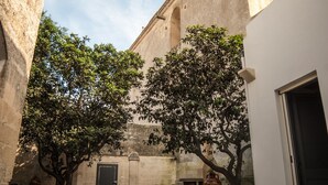 Un cortile con pavimentazione in pietra, un grande albero e un edificio con una torre.