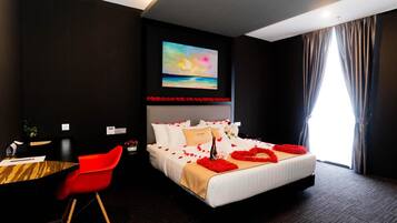 A hotel room with a large bed, a desk with a chair, a painting on the wall, and a window with curtains.