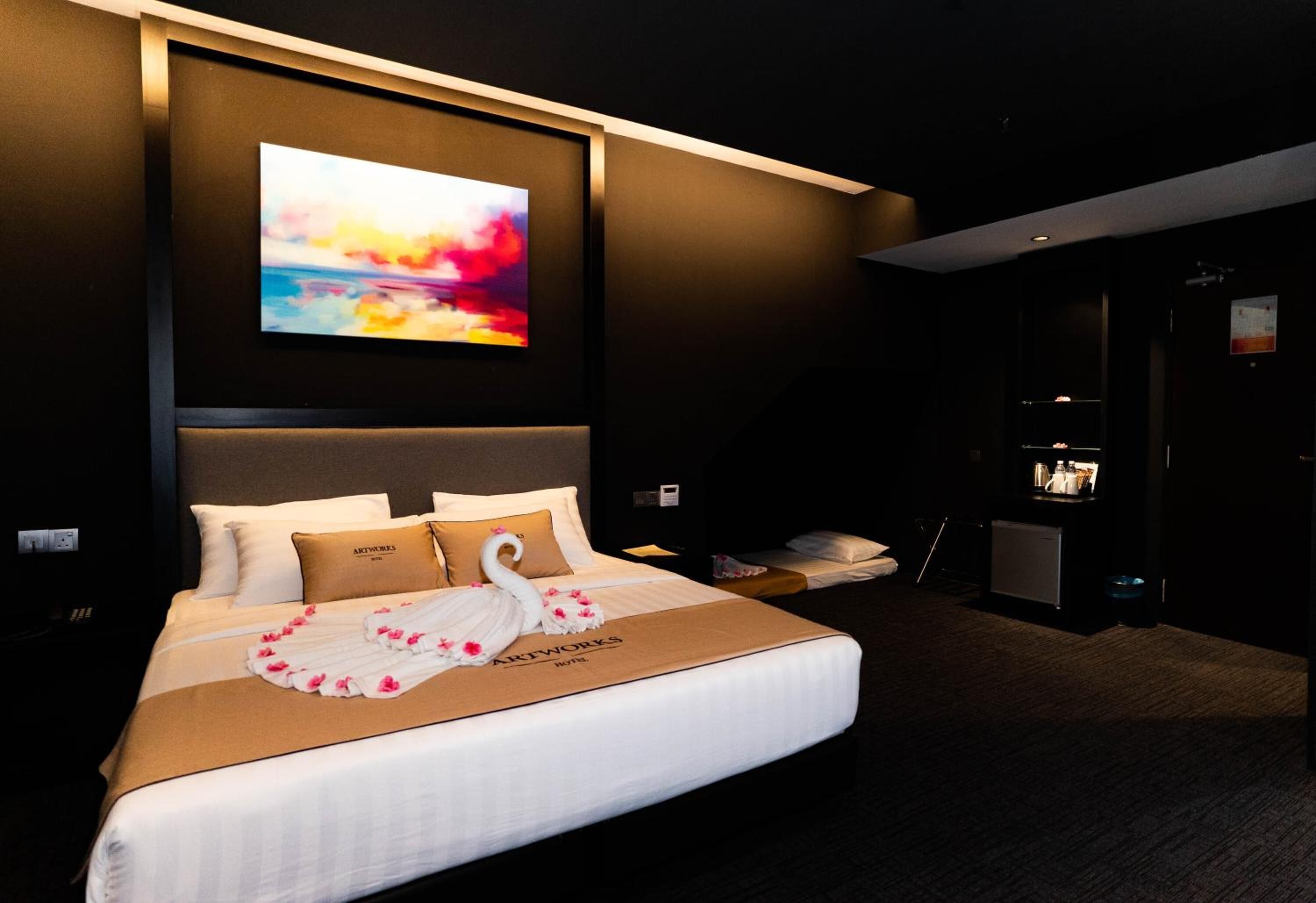 A modern hotel room with a large bed, a mounted TV, and a dark color scheme.