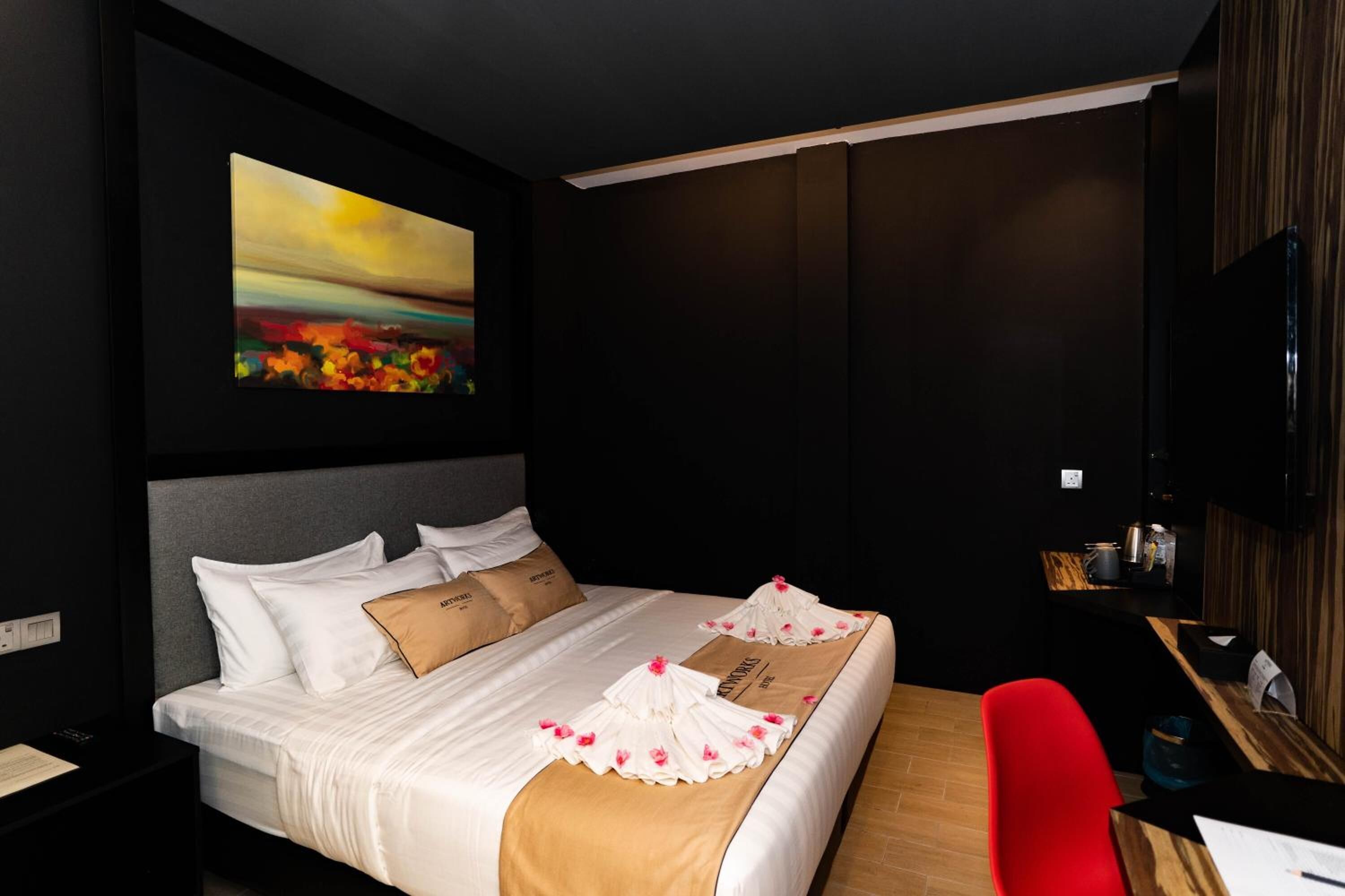 A hotel room with a bed, a desk, a chair, a painting on the wall, and a television.