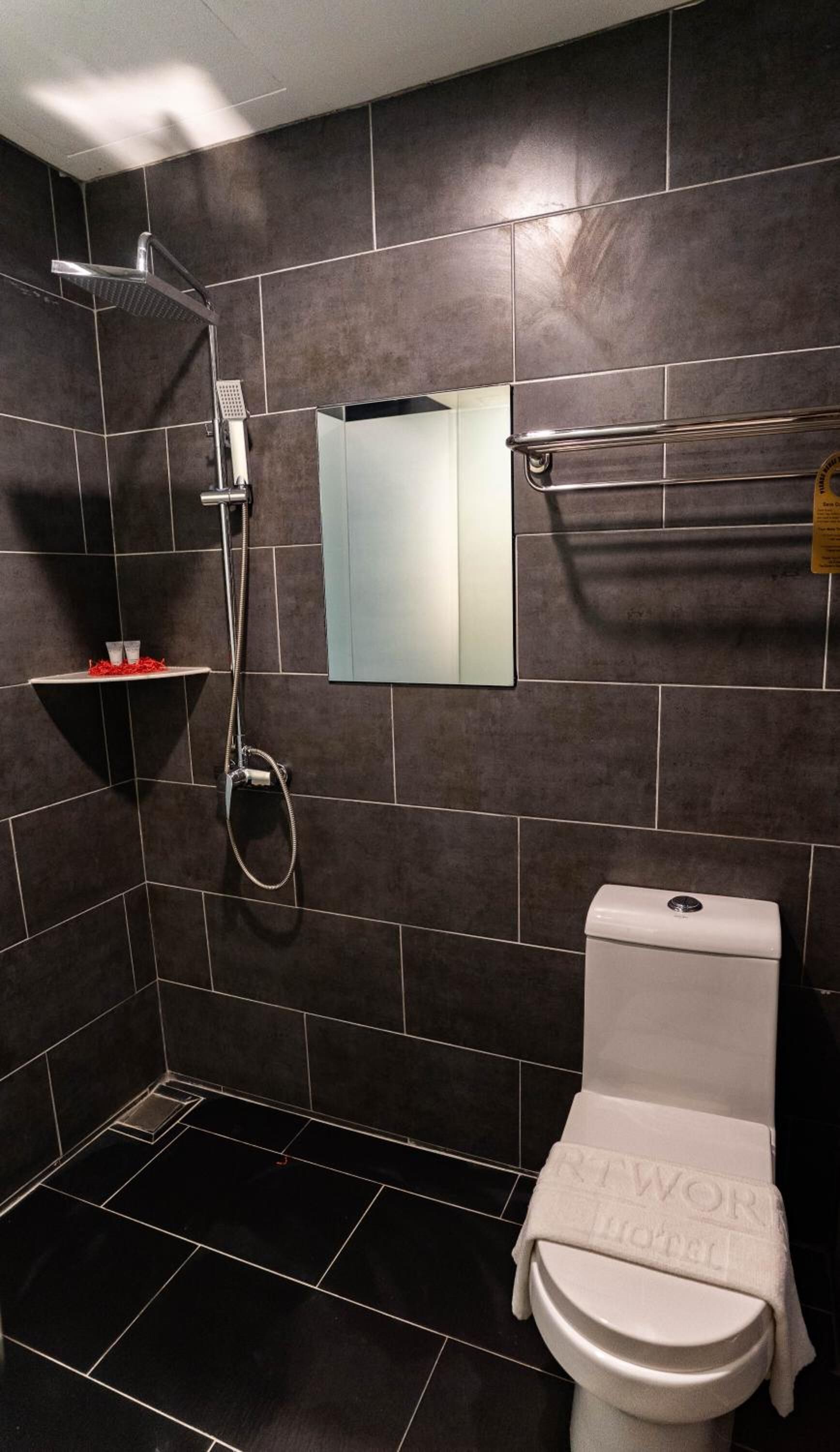 Een moderne badkamer met donkere tegels, toilet, douche en spiegel.