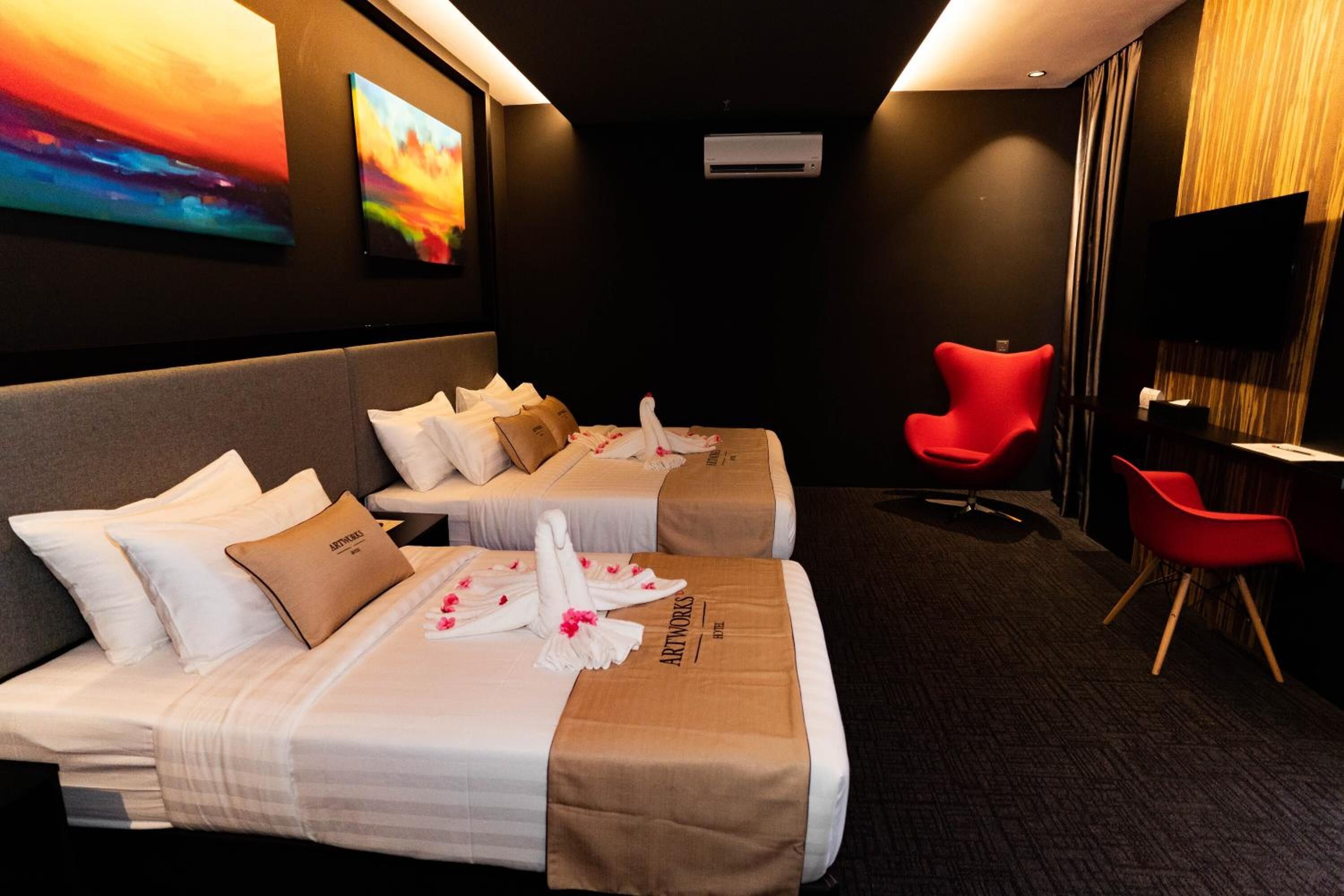 A hotel room with two beds, a red chair, a desk, and a TV.