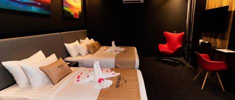 A hotel room with two beds, a red chair, a desk, and a TV.