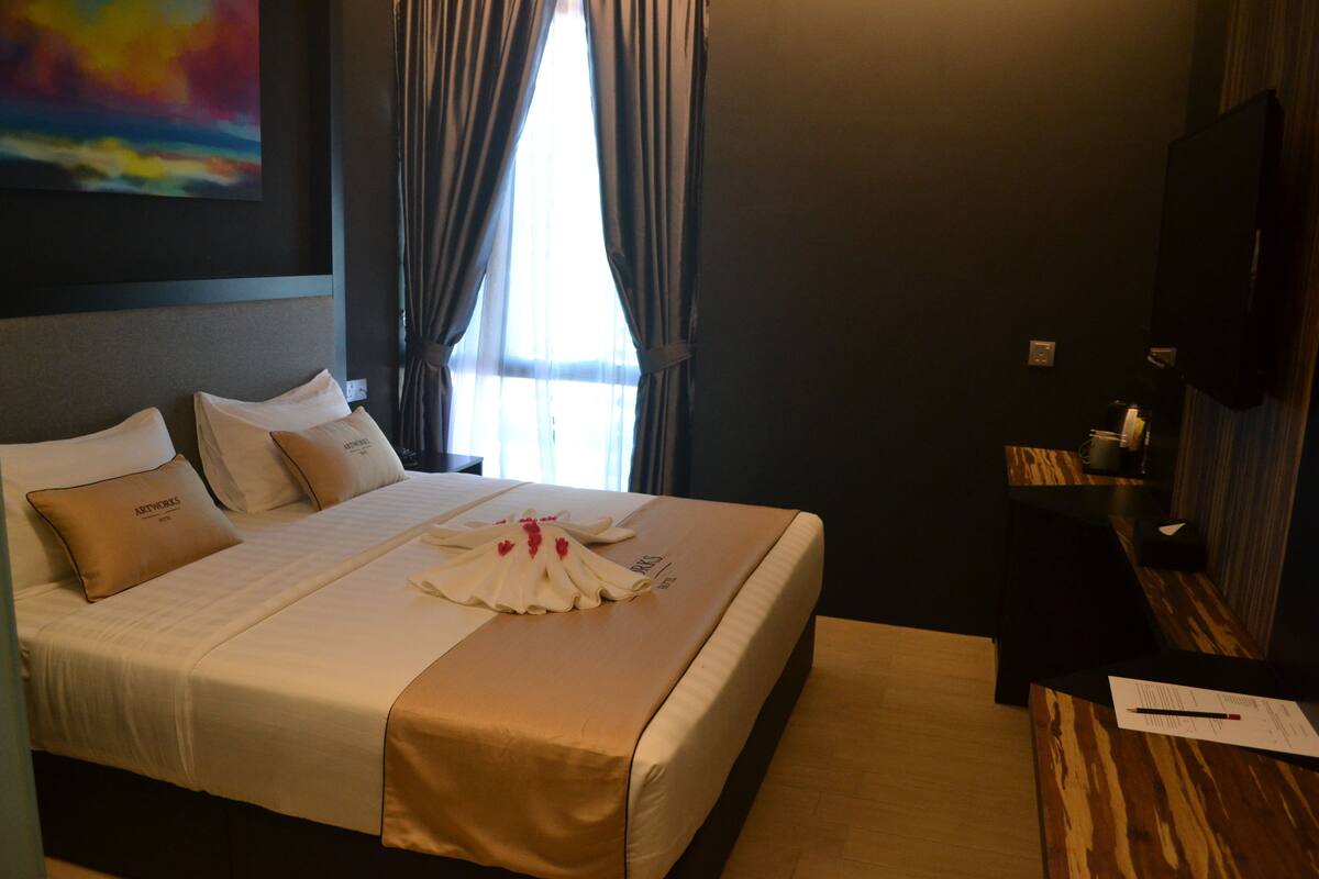 A hotel room with a large bed, a wooden nightstand, a flat-screen TV, and a painting on the wall.