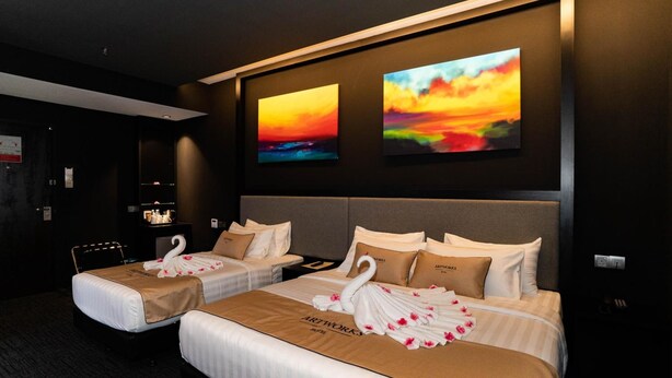 A hotel room with two beds, artwork on the wall, and a swan decoration on the beds.