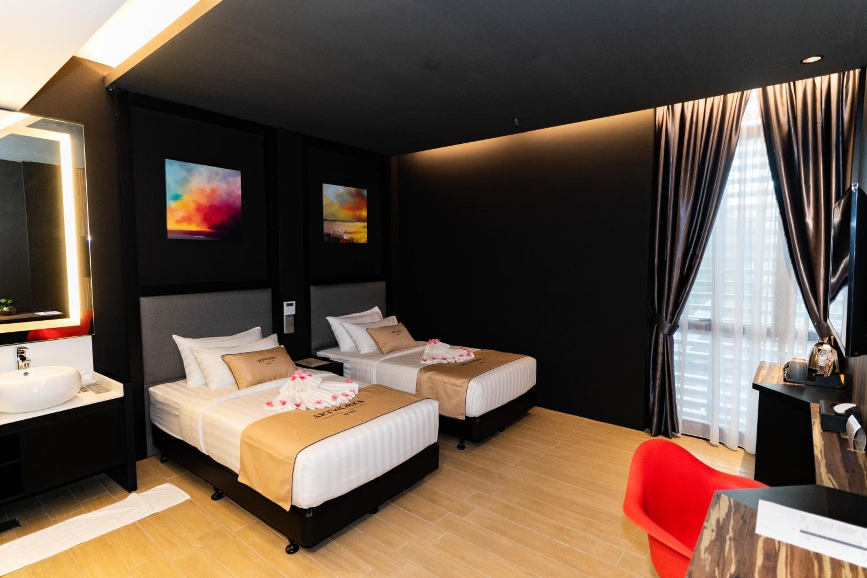 A hotel room with two beds, a red chair, a desk, and a large window with curtains.