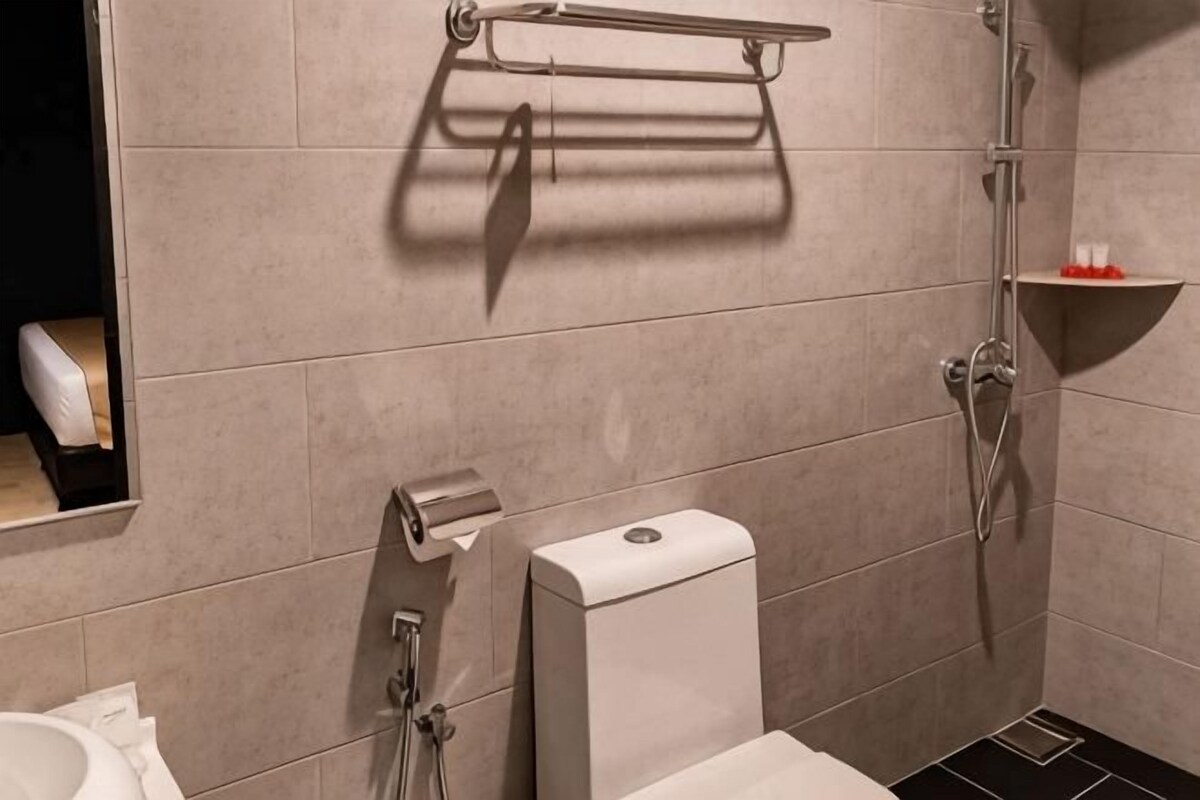 A bathroom with a toilet, a paper towel dispenser, a soap dispenser, a towel rack, and a shower area.