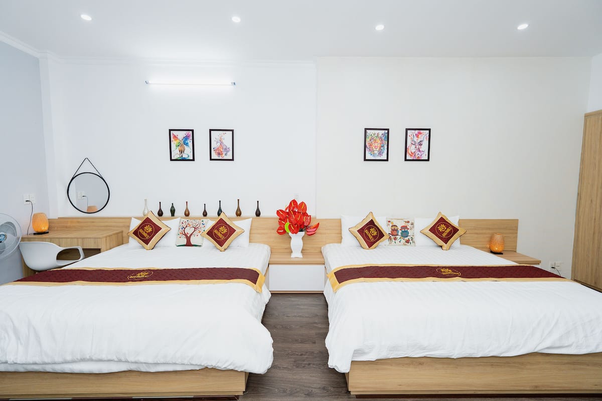 A hotel room with two beds, a wooden headboard, a bedside table with a vase of flowers, and framed artwork on the wall.