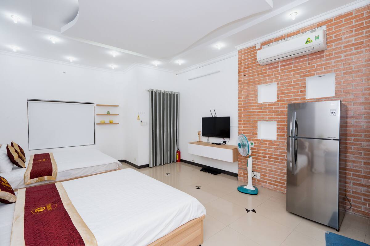 A hotel room with a large bed, a TV, a refrigerator, and a brick accent wall.