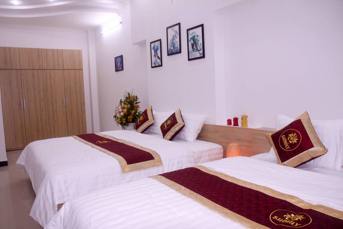 A hotel room with two beds, a wooden wardrobe, and three framed artworks on the wall.