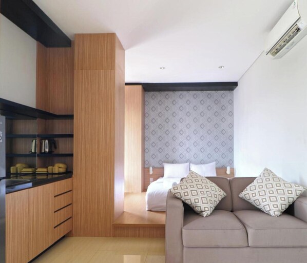 A compact room with a kitchenette, a bed with patterned pillows, and a sofa. - Plaza 54 Residence (Jakarta)
