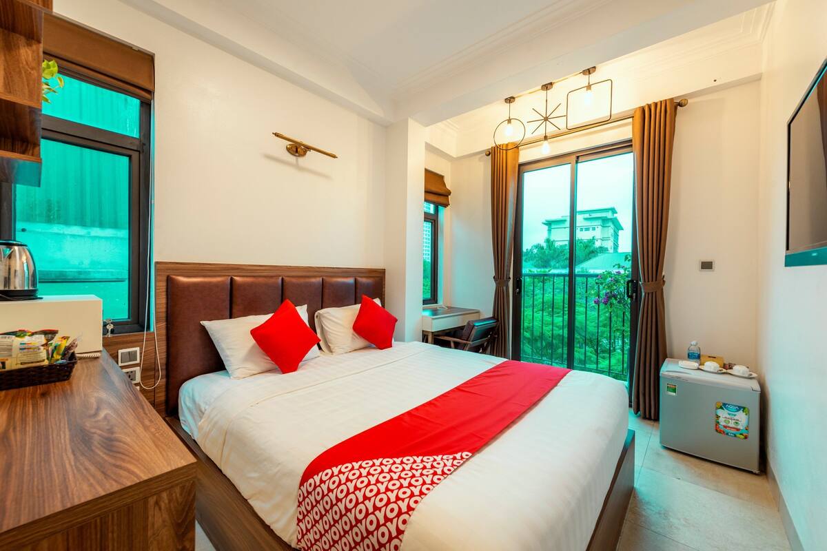 Une chambre d’hôtel avec un grand lit, un bureau, un réfrigérateur et une vue sur la verdure par la fenêtre.