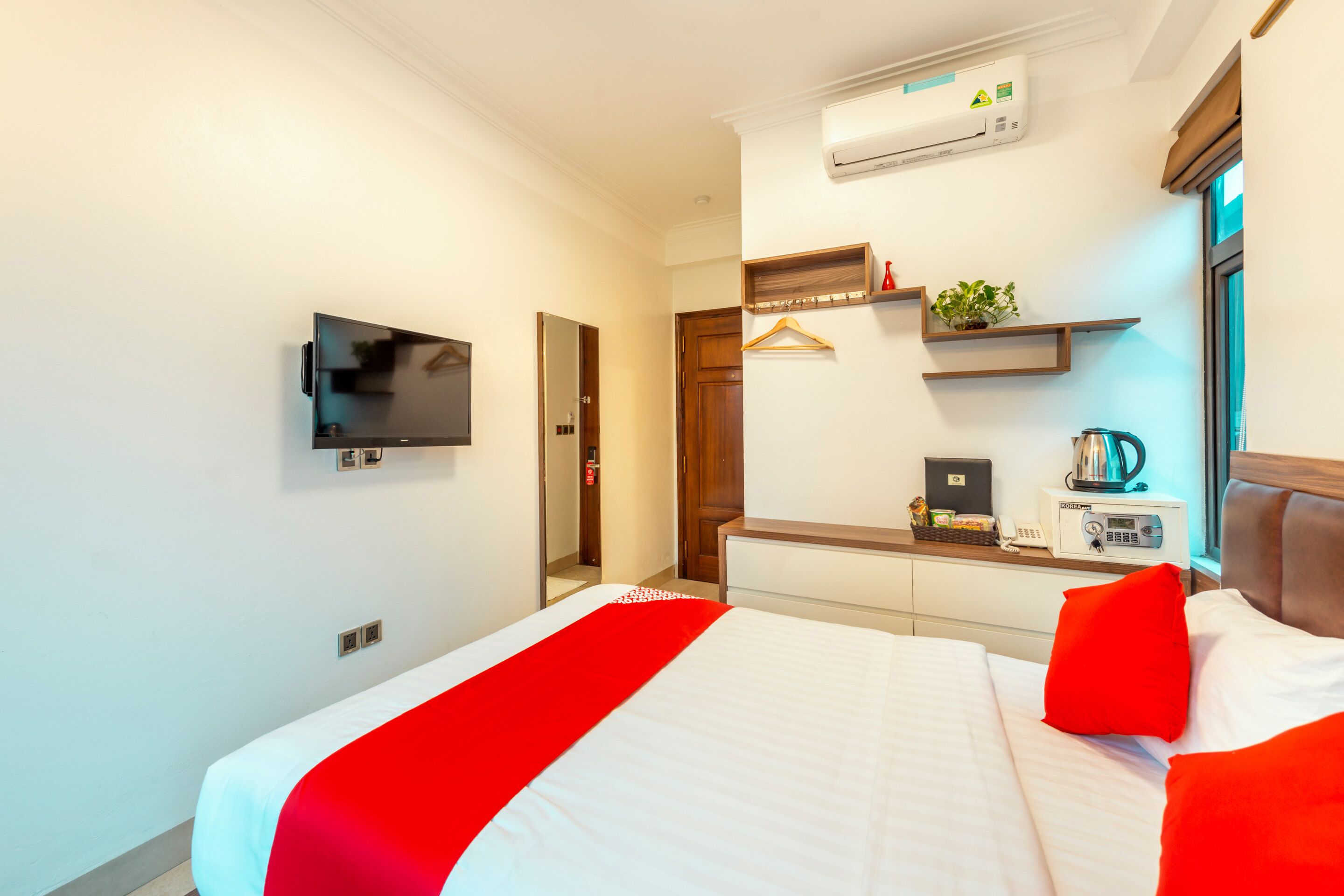 A hotel room with a bed, a TV, a desk with a coffee maker, and a window.