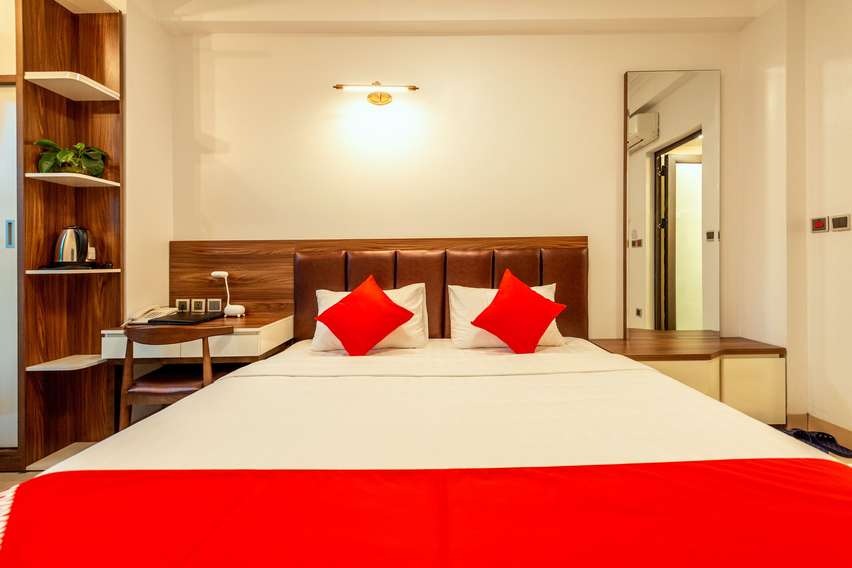 Ein modernes Hotelzimmer mit einem großen Bett, einem Holz-Kopfteil, Nachttischen, einem Beistelltisch, einem Spiegel und einem Regal mit einer Pflanze.
