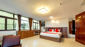 Ein Hotelzimmer mit einem großen Bett, einem Schreibtisch, einem Sessel und Blick ins Freie.