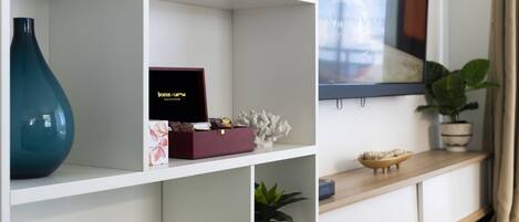 A modern living room with a white console table, a large flat-screen TV mounted on the wall, and a potted plant on the right side.