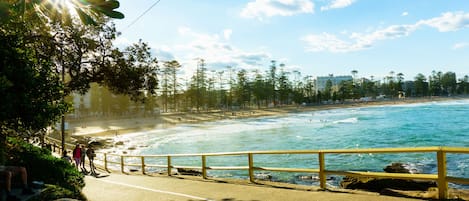 A coastal road with a yellow railing, leading to a beach with waves and a clear sky.