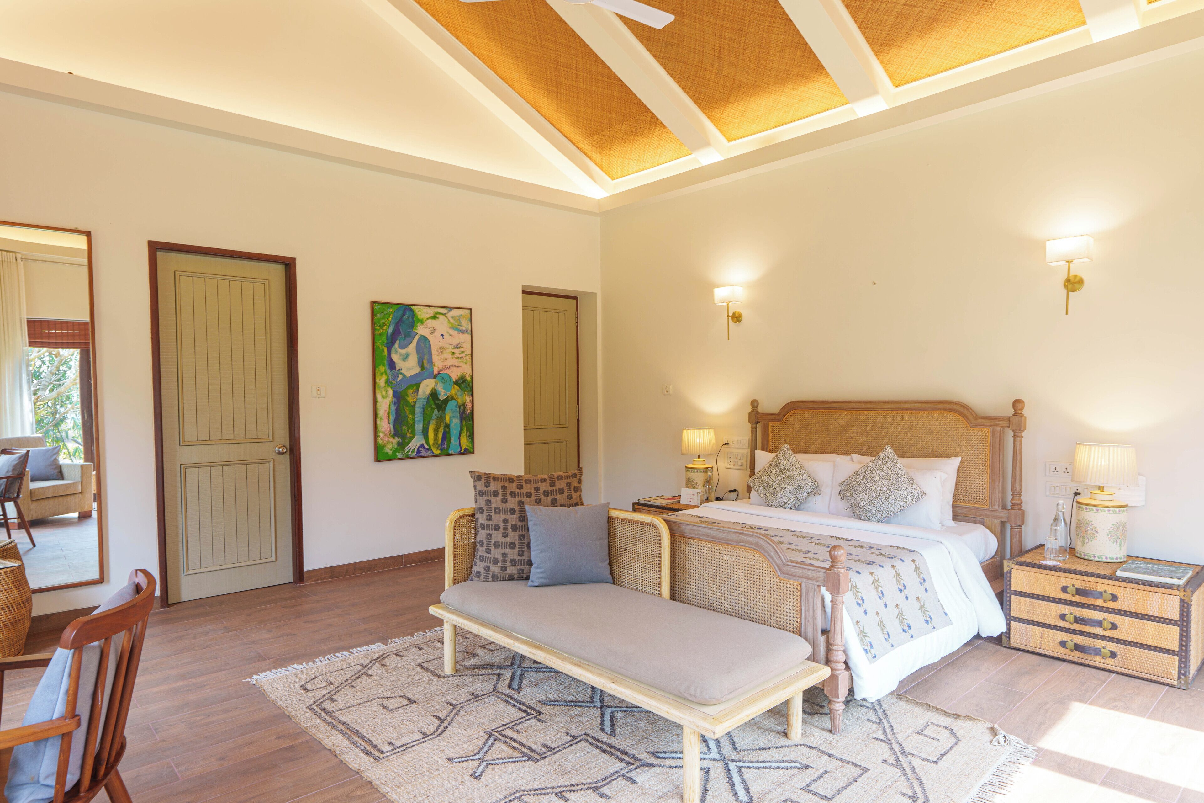 Un dormitorio con una cama, mesitas de noche, un banco, un cuadro y un ventilador de techo.