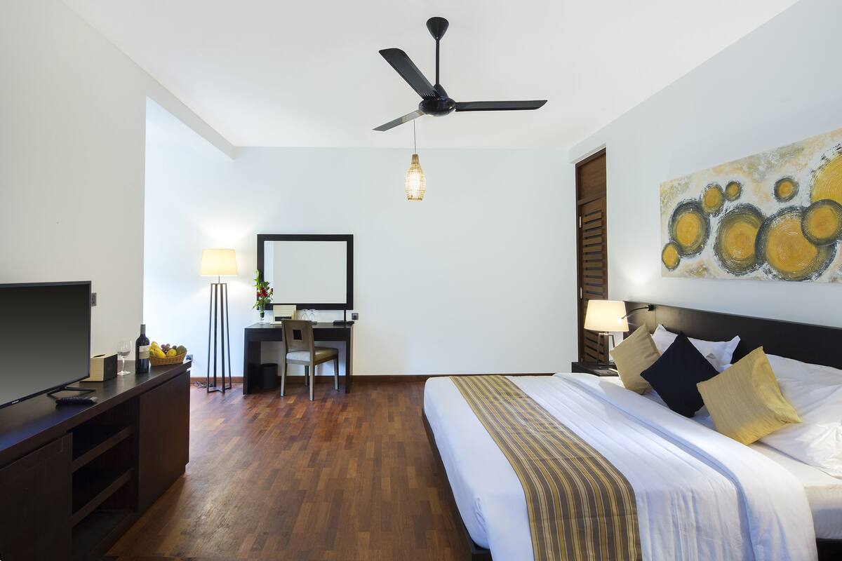 A hotel room with a bed, desk, television, and ceiling fan.