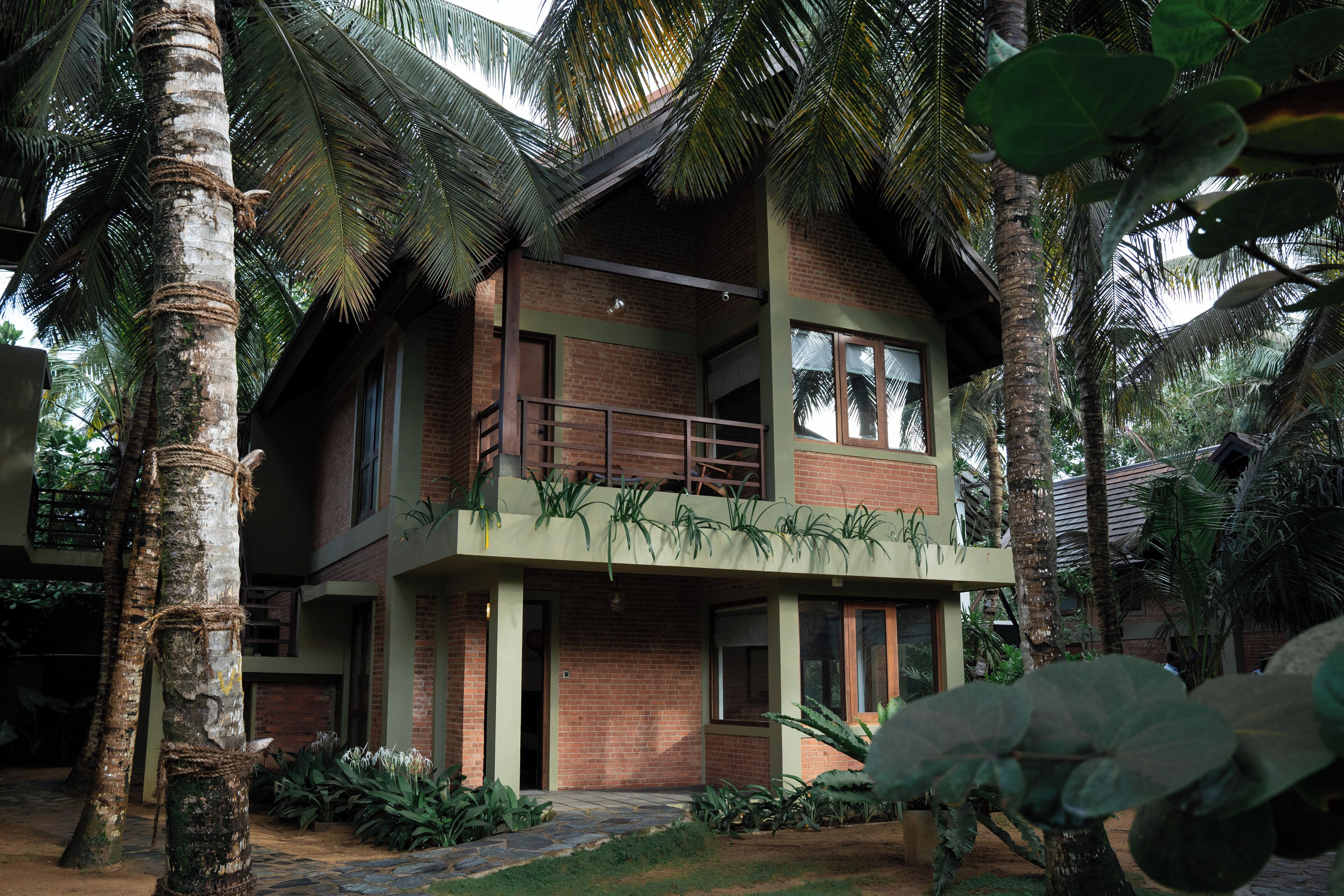 A two-story building with a balcony, surrounded by palm trees and greenery.
