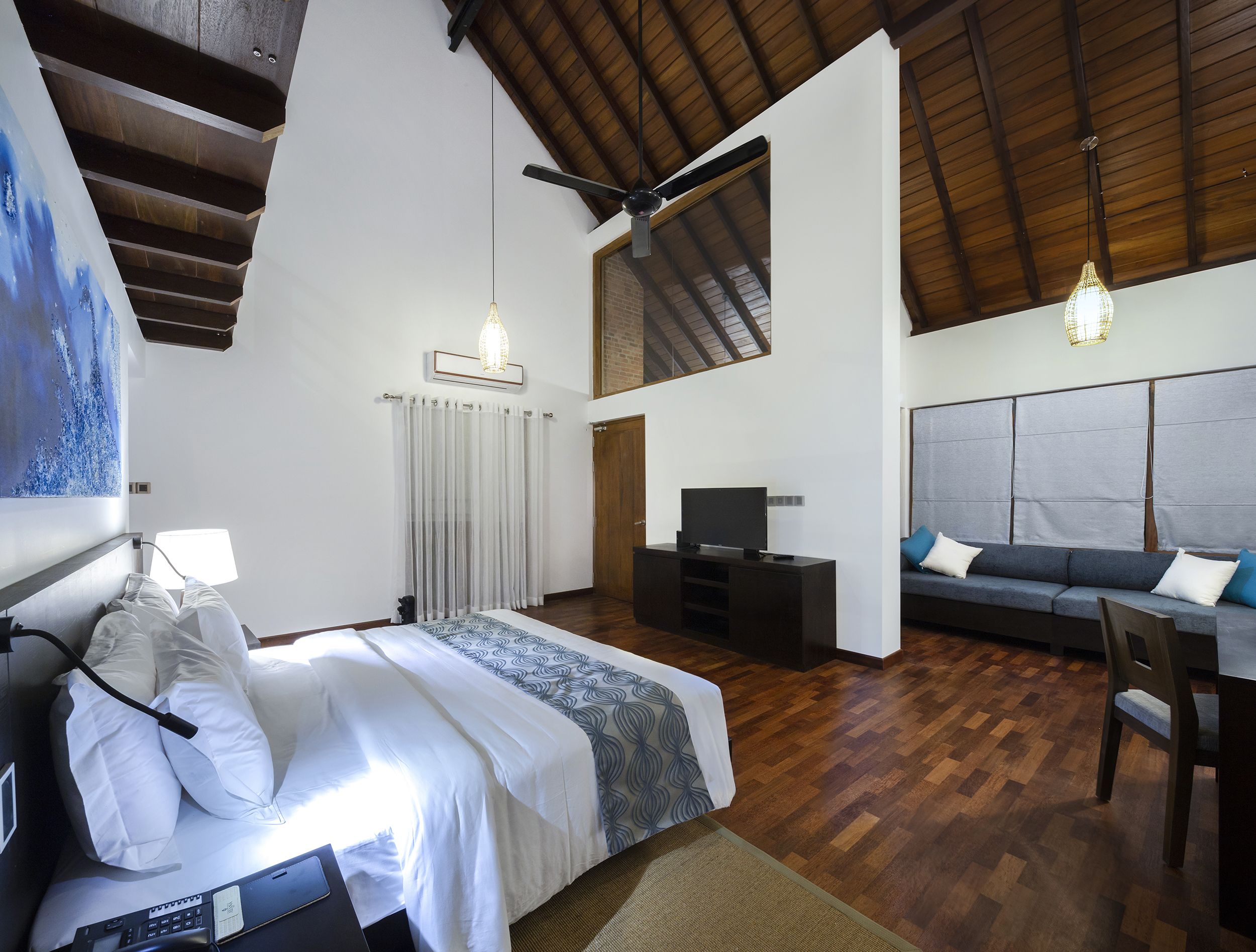 A spacious room with a large bed, a sofa, a TV, and a ceiling fan.