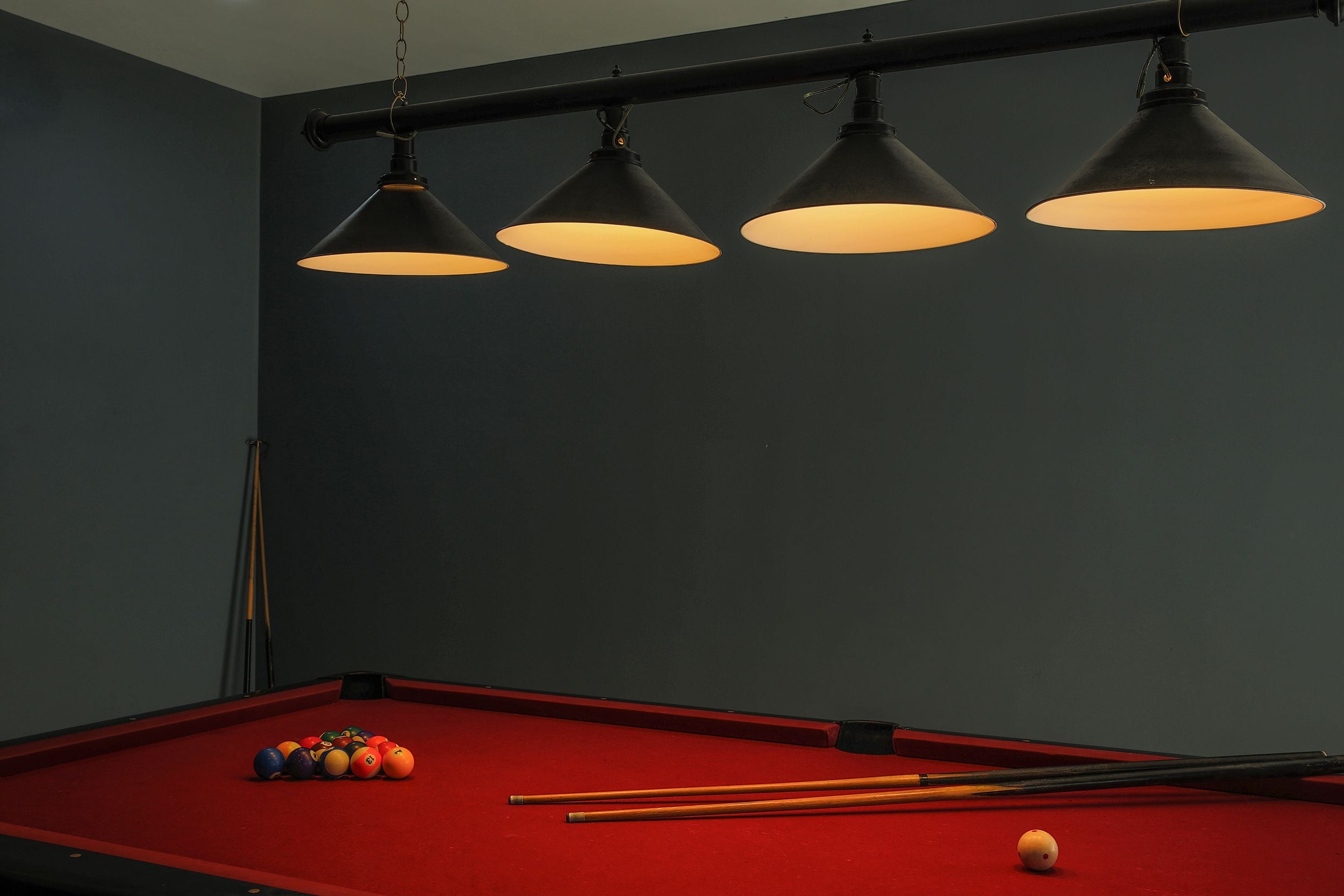 A pool table with balls and cues, three hanging lamps, and a dark wall.